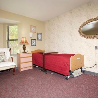 A cozy bedroom with a hospital bed, decorative mirror, and a comfortable chair by the window.
