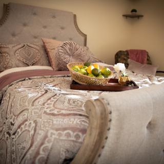 A cozy bedroom setting featuring a beautifully made bed with a fruit basket placed on top.