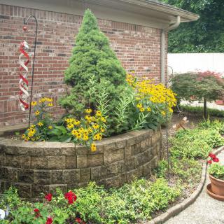 A beautifully landscaped garden with flowers and potted plants next to a brick wall.