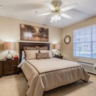 A cozy bedroom with neutral tones, featuring a neatly made bed, bedside tables with lamps, and a large window allowing natural light.