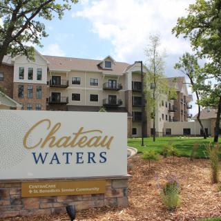 A residential building named Chateau Waters with a sign in the foreground surrounded by trees and landscaped grounds.