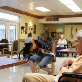 A person playing guitar for seniors in a nursing home setting.