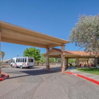 A bus parked under a covered entrance of a building on a sunny day.