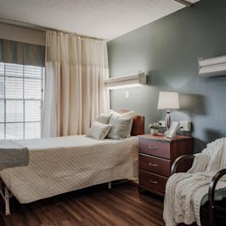 A serene hospital room featuring a neatly made bed, bedside table, and window with soft curtains.