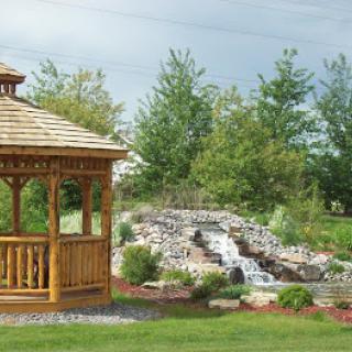 A serene garden scene featuring a wooden gazebo beside a tranquil waterfall.
