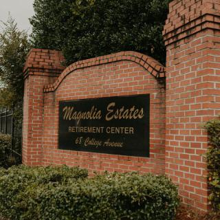 Entrance sign for Magnolia Estates Retirement Center, mounted on a brick wall surrounded by greenery.