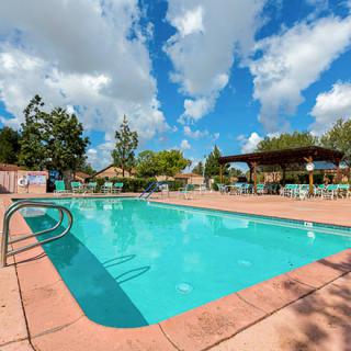An outdoor swimming pool with surrounding chairs and tables under a partly cloudy sky.