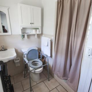A small bathroom with a commode chair, sink, and shower curtain.