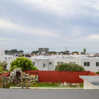 A suburban neighborhood with white houses, a red fence, and lush gardens under a cloudy sky.