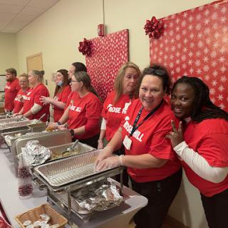 A group of volunteers in red shirts serving food at a community event.