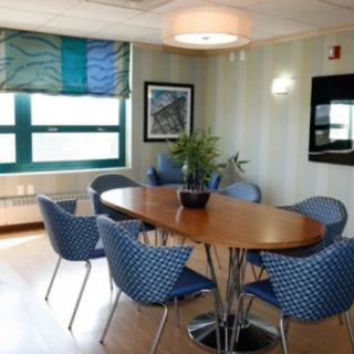 A modern conference room with a wooden table, blue chairs, and large windows.