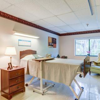 A well-lit hospital patient room featuring a bed, bedside table, and a comfortable chair.