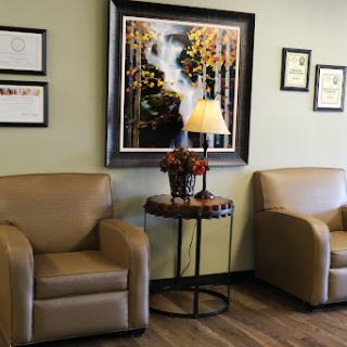 A cozy waiting area featuring comfortable seating, a decorative table with flowers, and an artistic wall piece.