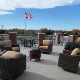 An outdoor patio featuring wicker chairs and a table, with an American flag waving in the background under a clear sky.