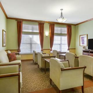 A cozy living room with several chairs and sofas arranged around a television, featuring elegant curtains and a carpeted floor.