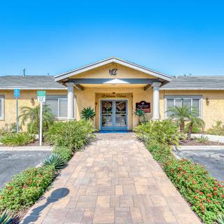 A welcoming building entrance with a paved pathway and well-maintained landscaping under a clear blue sky.