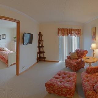 A cozy living room with pink upholstered furniture and a view into the adjacent bedroom.