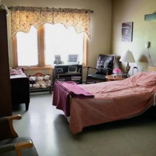 A hospital room with a bed, furniture, and a window with curtains.