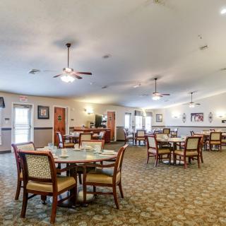 Spacious dining area with multiple tables and chairs, ceiling fans, and carpeted flooring.