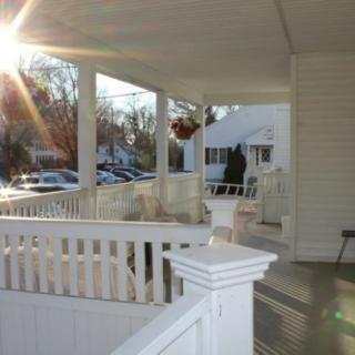 A sunlit porch with white railings and a view of parked cars in the background.