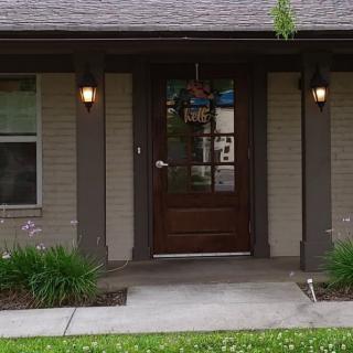 A welcoming front entrance of a house with a wooden door, porch lights, and landscaped greenery.