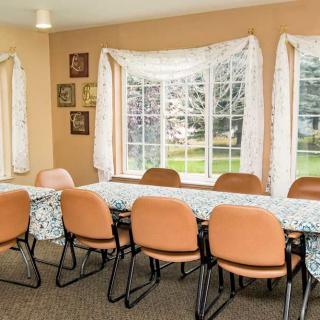 A meeting room with orange chairs around tables, featuring large windows with curtains.