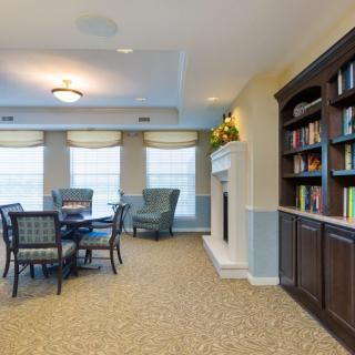 A cozy living room with a library, featuring bookshelves, a fireplace, and a seating area with a table and chairs.