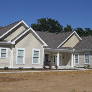 A newly constructed suburban house with beige siding and a large front porch.