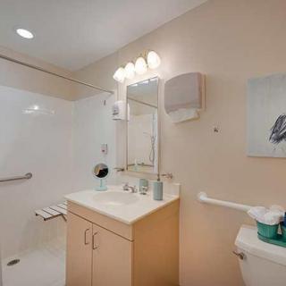 A modern bathroom featuring a sink, mirror, and toilet, with a walk-in shower and bright lighting.