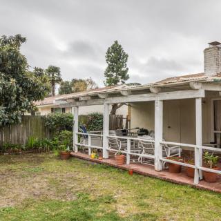 A backyard with a covered patio and outdoor furniture, surrounded by a lawn and garden.