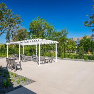 A patio area with a pergola and outdoor seating surrounded by greenery under a clear blue sky.
