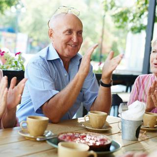 A group of seniors clapping and enjoying coffee at an outdoor cafe.