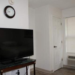 A minimalist living room featuring a television, a clock on the wall, and a door.