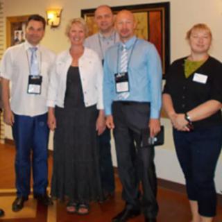 A group of five people posing together at an indoor event, wearing formal attire and conference badges.