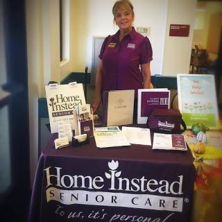 A representative from Home Instead Senior Care standing by an informational booth, highlighting services provided for senior care.