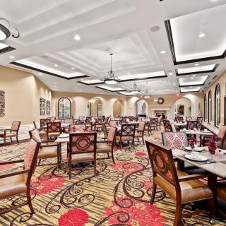 An elegant restaurant dining room with beautifully arranged tables and chairs, featuring a decorative carpet and stylish lighting.