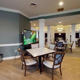 A well-furnished dining area with multiple tables, chairs, and a television, featuring elegant lighting and hardwood floors.