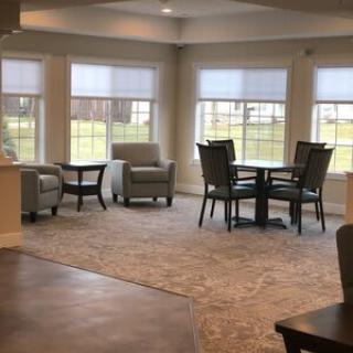 A cozy living room with chairs and a table near large windows letting in daylight.
