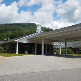 A modern building set against a backdrop of green hills and cloudy skies.