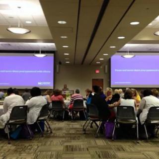 A group of people seated in a conference room facing two large screens during a presentation.