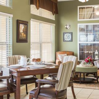 A cozy dining area with a wooden table, upholstered chairs, and abundant natural light streaming through multiple windows.