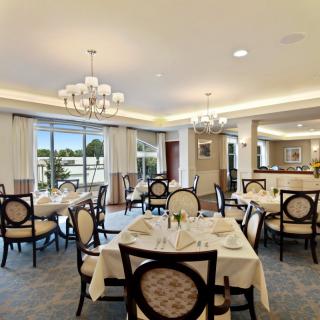 An elegant dining room with neatly arranged tables and chairs, adorned with chandeliers and large windows providing ample natural light.