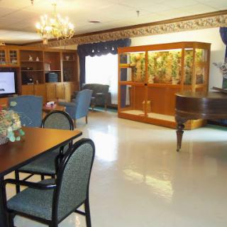 A spacious and elegantly furnished living room with a dining area, a grand piano, and a beautifully arranged wooden cabinet.