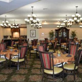 An elegant dining room with neatly arranged tables and chairs, illuminated by decorative chandeliers.