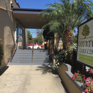 Entrance of a care center with palm trees and decorative flowers.