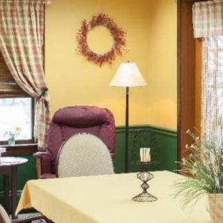 A cozy living room with a purple chair, floor lamp, and table near a window with curtains.