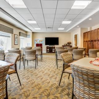 A well-lit meeting room with tables and chairs arranged neatly, featuring a television on the wall.