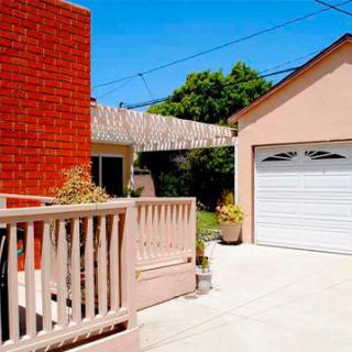 A sunny day in a suburban neighborhood featuring a house with a brick exterior, an adjacent garage, and a spacious driveway.