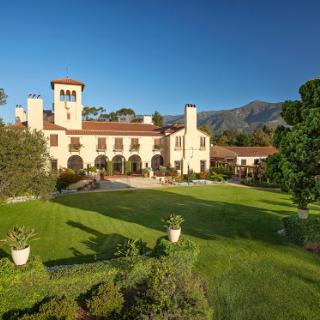 A beautiful mansion set in a lush green landscape under clear blue skies.