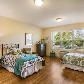 A cozy bedroom with two beds, stylish decor, and a large window overlooking greenery.